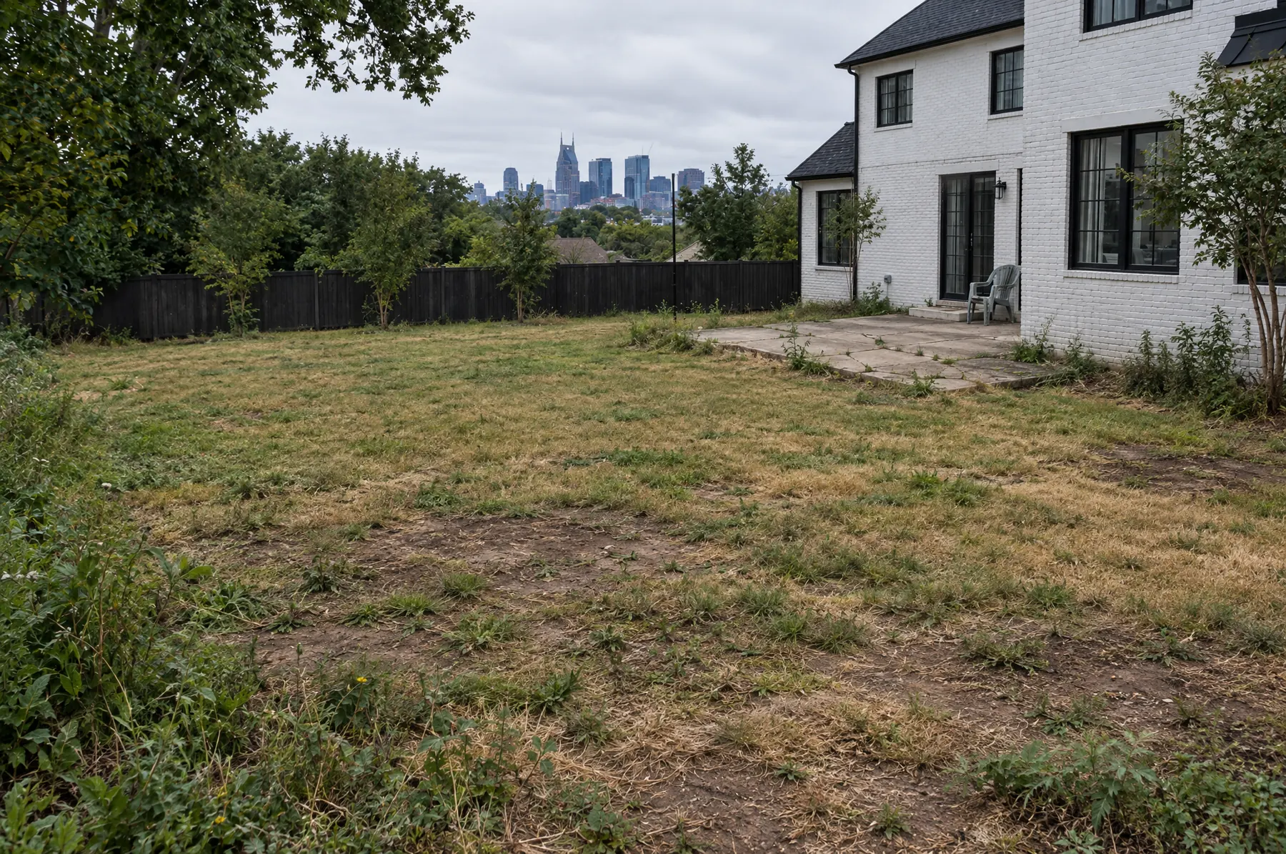 The backyard before: patchy brown lawn, cracked concrete slab