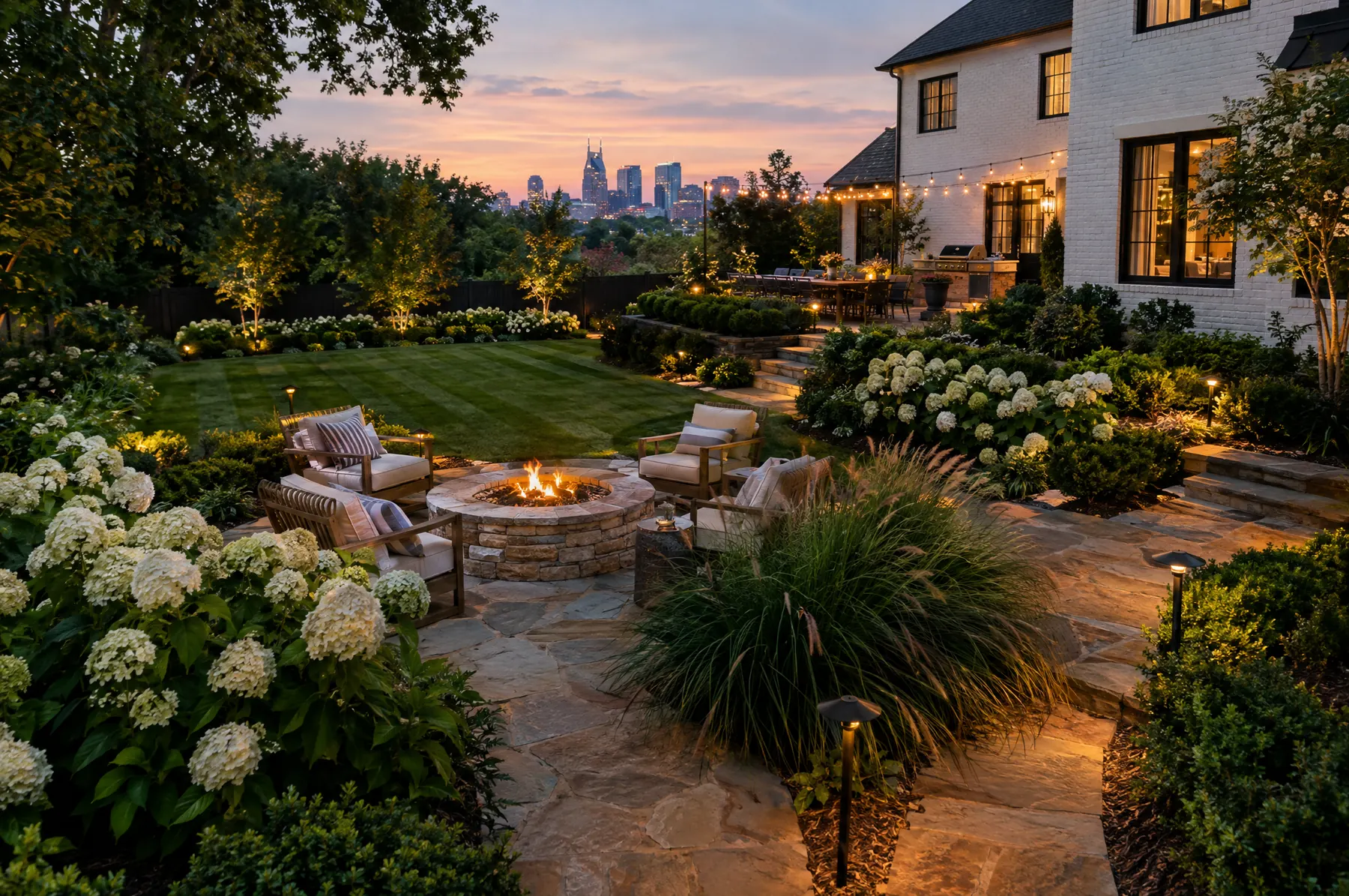 A Fernhill backyard at dusk: flagstone patio, fire pit, hydrangeas and lit paths with the Nashville skyline behind